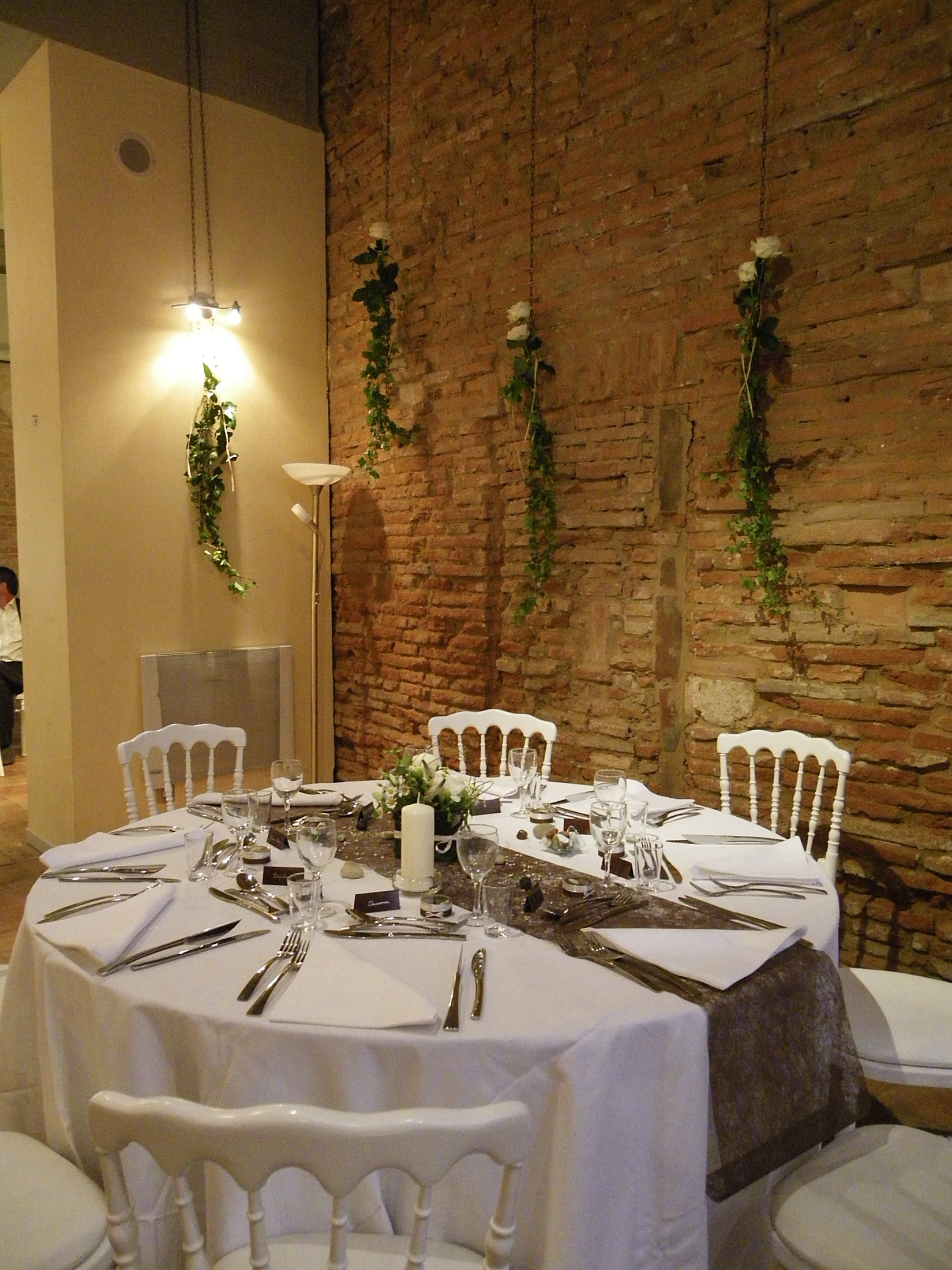Table de mariage dressée, guirlandes de lierre et roses sur le mur de brique
